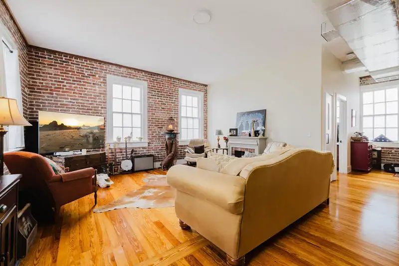 Living room in Apartment 301 with exposed brick walls, two tall windows and original hardwood floors