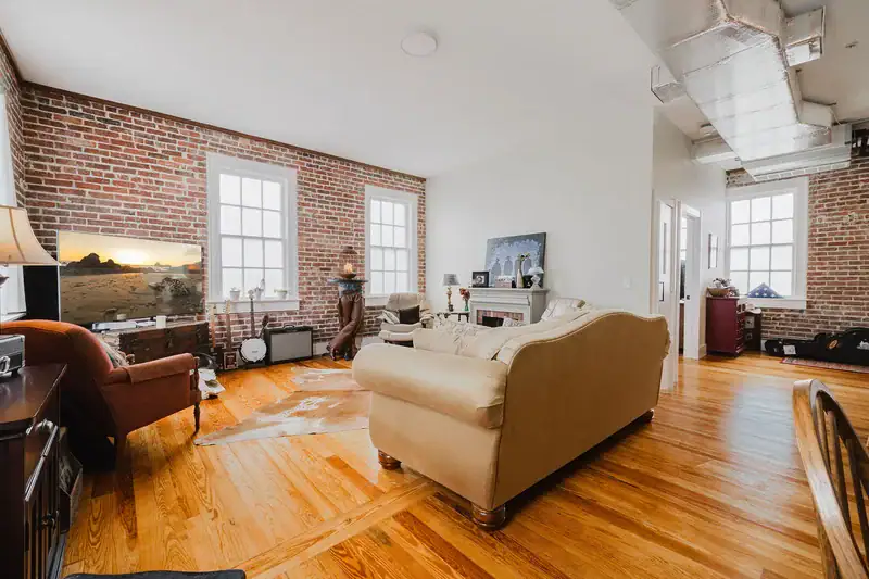 Wide view of the living room in Apartment 301 with brick walls, hardwood floors and exposed ductwork