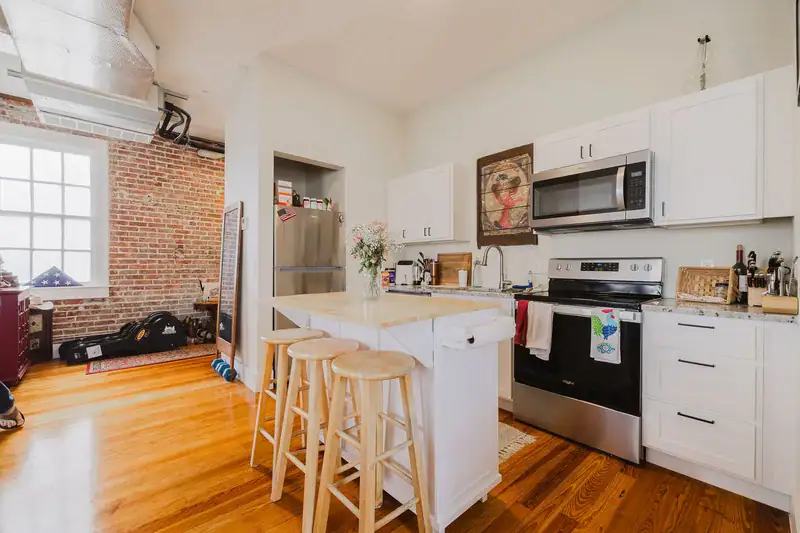 Kitchen in Apartment 301 with a breakfast bar and stools, stainless range and microwave, and brick wall beyond