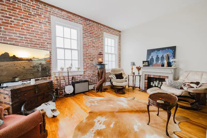 Living room in Apartment 301 with a brick wall, two windows and a decorative fireplace