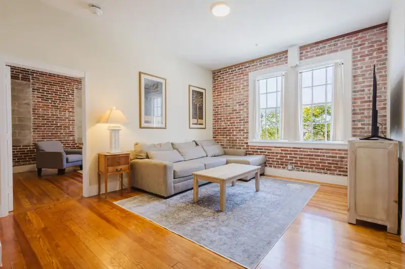Apartment 303 living room with sectional sofa, exposed brick wall and view into the bedroom