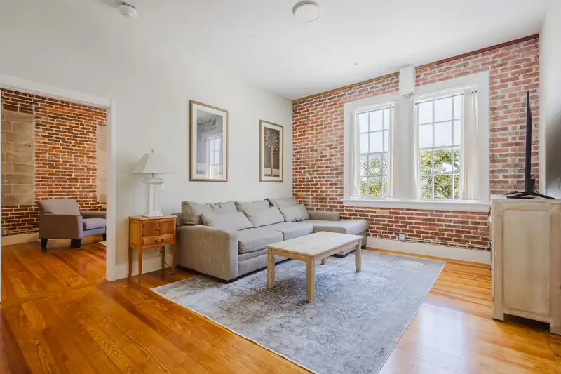 Apartment 303 living room with sectional sofa, exposed brick wall and tall windows
