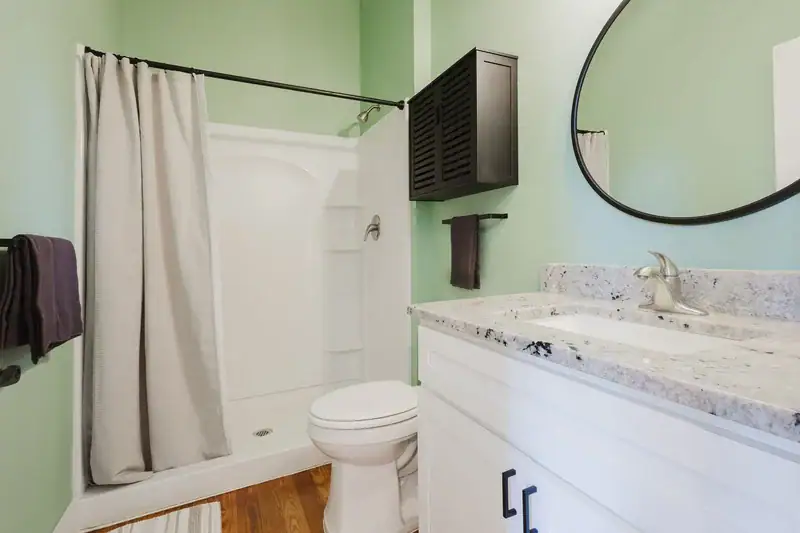 Apartment 303 bathroom with green walls, round mirror and granite vanity