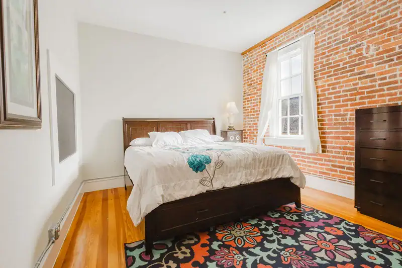 Apartment 303 bedroom with wood bed frame, floral rug and exposed brick