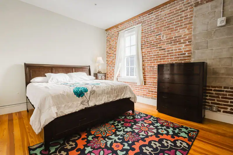 Apartment 303 bedroom with wood dresser and exposed brick wall