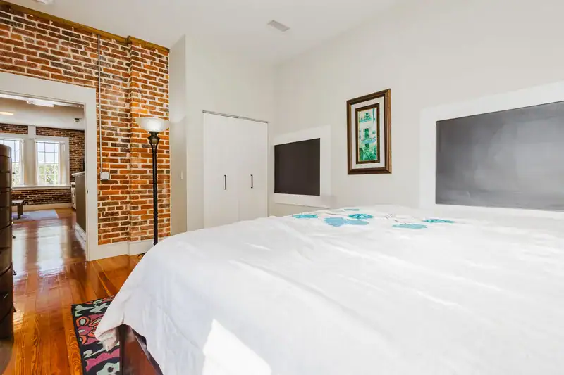 Apartment 303 bedroom with white bedding and exposed brick