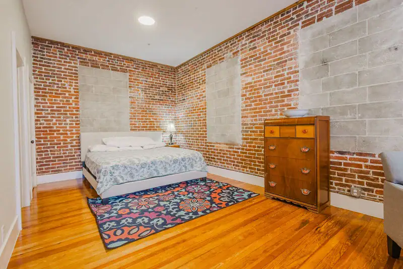Apartment 303 bedroom with bed, wood dresser and exposed brick