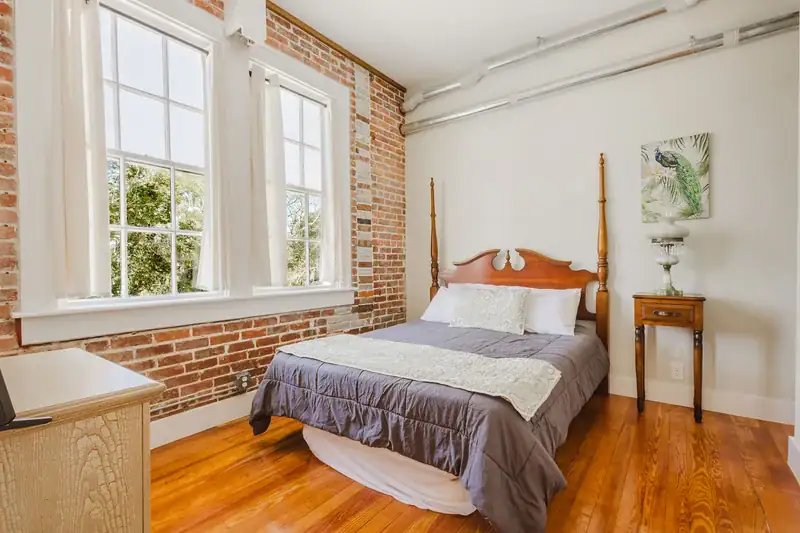 Apartment 303 bedroom with exposed brick wall and tall windows